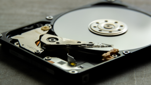 Close-up of an open hard drive, showing the reflective circular disk and mechanical arm. The image conveys a technical and precise tone.